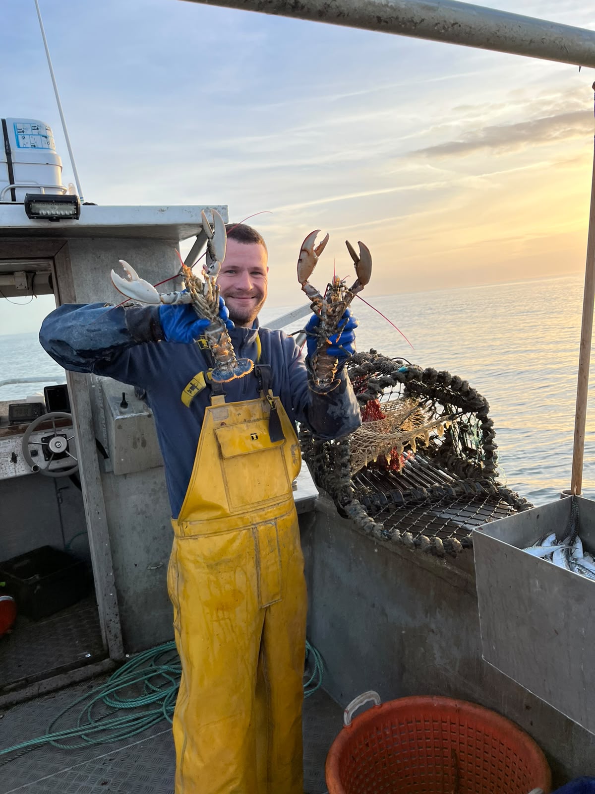 Alban tenant deux homards au retour de casiers, au coucher de soleil